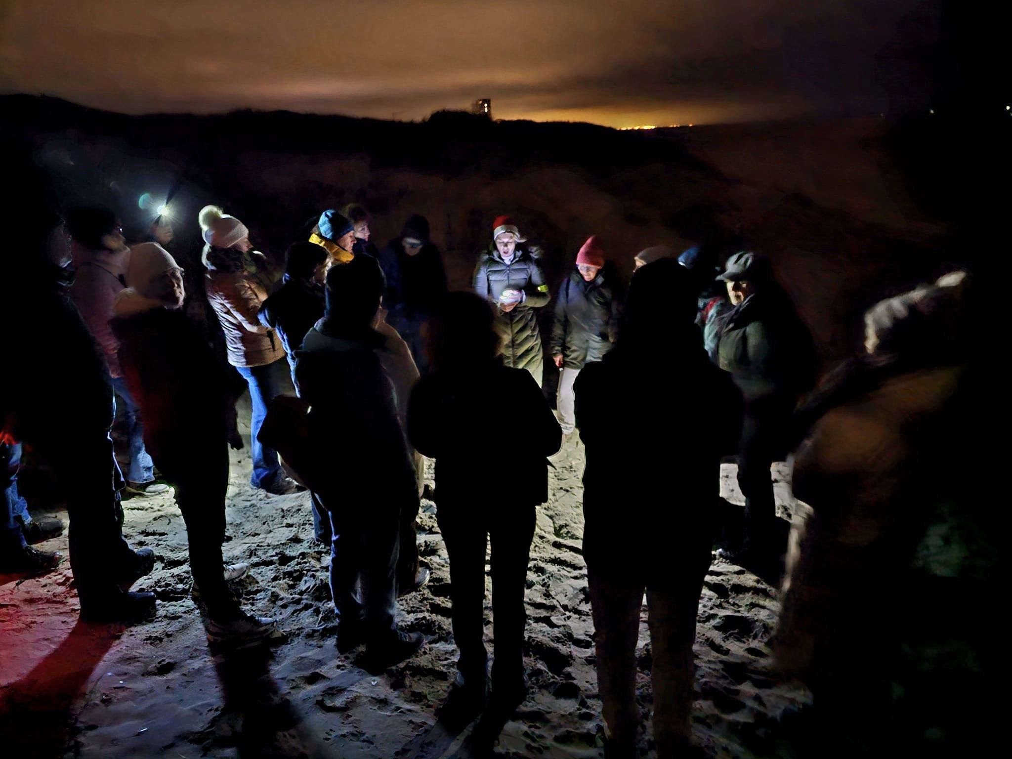 groep mensen in het donker op het strand tijdens de moonwalk