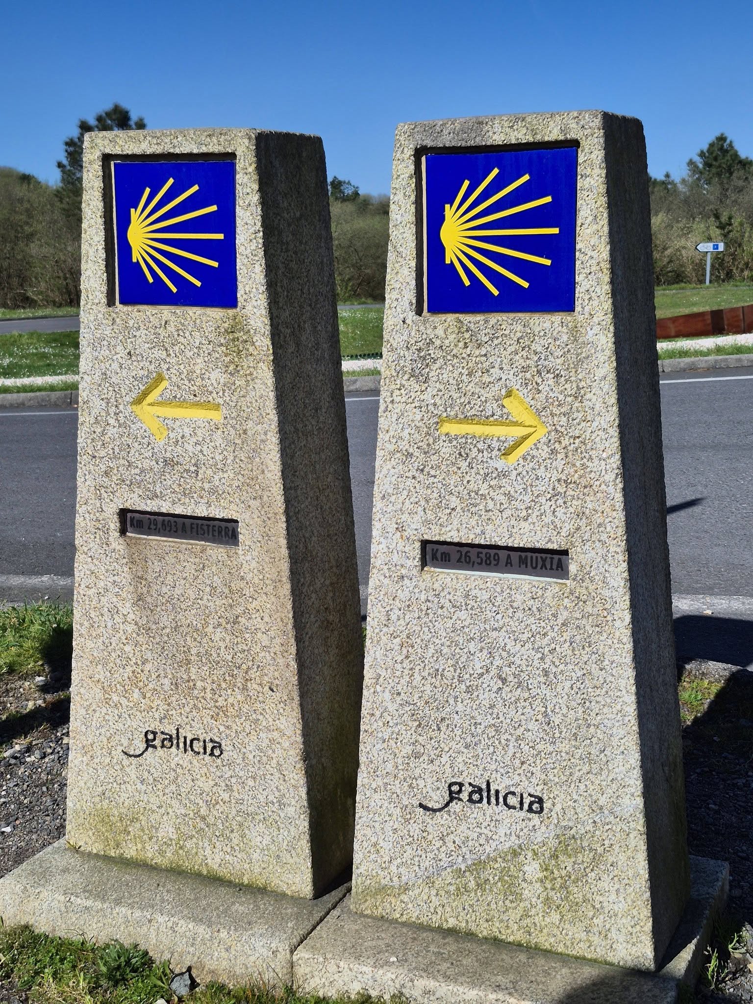 camino pijlen, gele schelp met zonnestraal motief tegen blauwe achtergrond