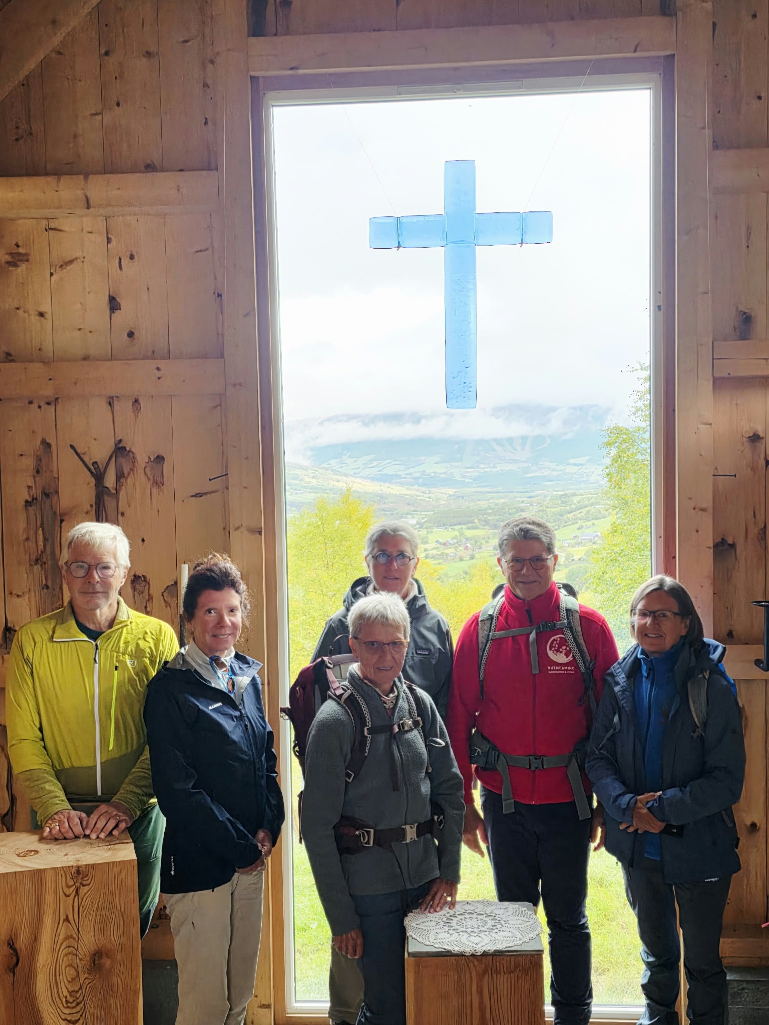 wandelaars in houten kerkje in noorwegen, met simpel kruis in blauw glas in de achtergrond